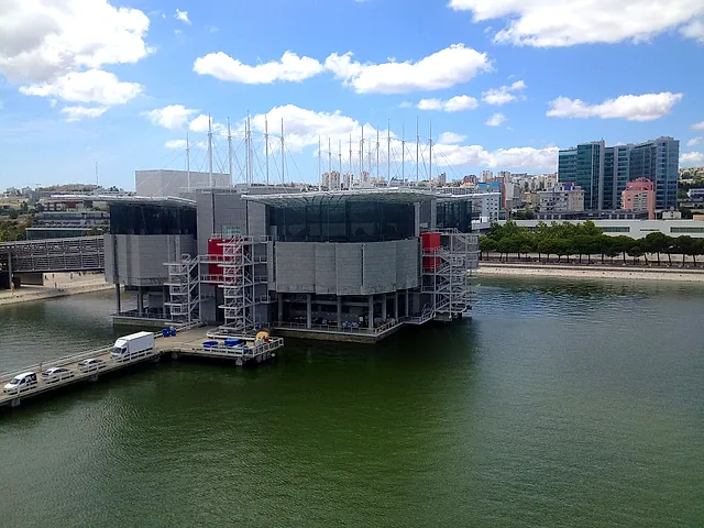 L'Oceanário di Lisbona visto dall'altra parte dell'acqua sotto un cielo azzurro, con gli edifici del Parque das Nações dietro